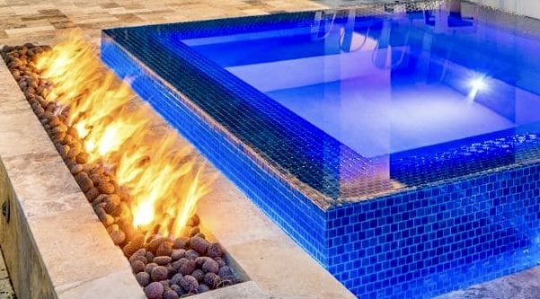 Glass-tile spa lit blue beside a linear fire feature